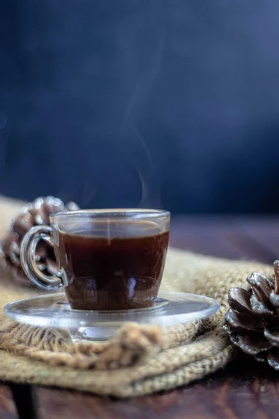 Coffee in a transparent cup. Hot, invigorating drink. Near cones in sparkles, coffee beans are scattered.