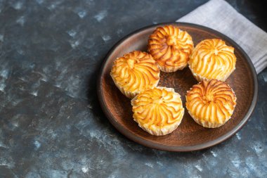 Kahverengi bir kil plaka üzerinde krem dolgulu cupcakes vardır. Arka planda gri, bez peçete var. Her şey karanlık bir arka plan üzerinde yer almaktadır