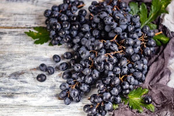 Large, black, wine grapes. It is covered with a white coating called yeast. With the help of them, wine is obtained. Drops of water on the berries, next to a gray fabric for decoration.