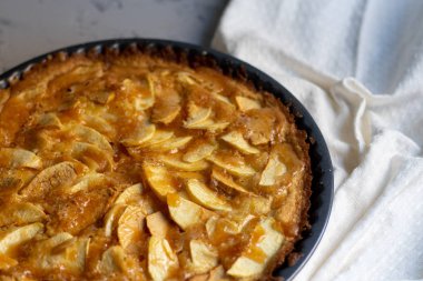 Yuvarlak şekilli elmalı turta, vantilatör katkılı elma dilimleri ile süslenmiş, bir fincan sıcak çay, sonbahar yaprakları, hepsi açık renkli, mermer gri arka plan. 