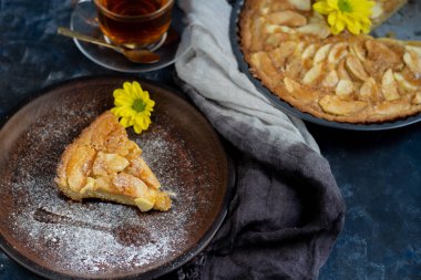 Yuvarlak şekilli Charlotte elmalı turtası, vantilatör katılmış elma dilimleri, yanında bir parça kek, bir fincan çay, sonbahar yaprakları, hepsi koyu bir arka planda.. 
