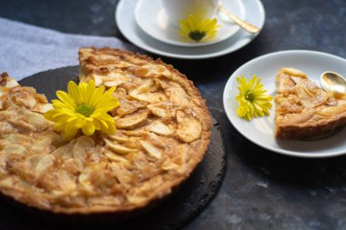 Yuvarlak şekilli Charlotte elmalı turtası, vantilatör yüklü elma dilimleriyle süslenmiş, yanında bir parça kek, bir fincan kahve, sonbahar yaprakları, hepsi koyu bir arka planda.. 