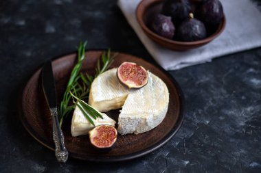 Olgun, güzel, mor incirler. Tatlı ve sulu. Akdeniz meyvesi çok sağlıklıdır. Tabakta Brie peyniri var. Karanlık bir telif uzayı arka planında boş bir alan var. Vejetaryenler için yiyecek..