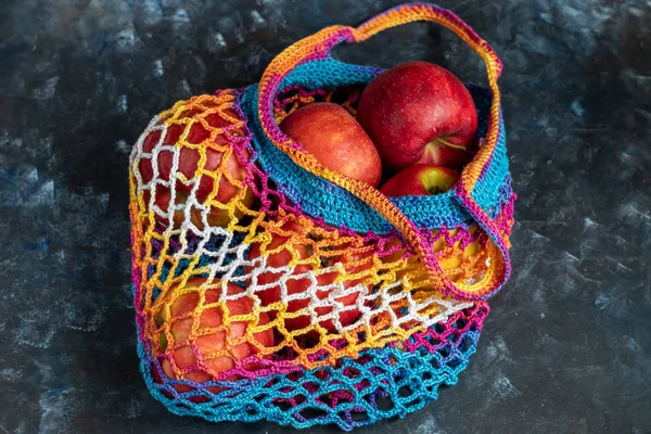 Ecological cotton mesh for carrying and storing products. Durable, bright. In a mesh bag are fruits. Red apples. View from above. On a bright background. Copy space.