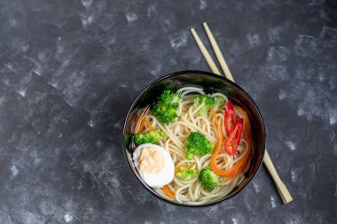 Buğday erişteli Asya çorbası, bir dilim et, kırmızı biber. Nane yaprağı, fesleğen, yeşil soğan tüyü ile süslenmiş. Havuç ve brokoli var. Sağlıklı, beslenme ürünü. Boşluğu kopyala. 