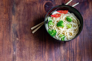 Buğday erişteli Asya çorbası, bir dilim et, kırmızı biber. Nane yaprağı, fesleğen, yeşil soğan tüyü ile süslenmiş. Havuç ve brokoli var. Sağlıklı, beslenme ürünü. Boşluğu kopyala. 