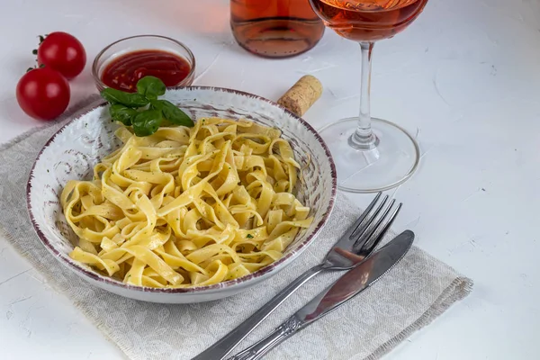 Italian pasta, spaghetti with avocado, spinach, basil, cream, cheese. Vegetarian vegetable pasta. Spinach with noodles. On a light background. In the background is a glass of orange wine. Copy space.