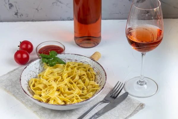 Italian pasta, spaghetti with avocado, spinach, basil, cream, cheese. Vegetarian vegetable pasta. Spinach with noodles. On a light background. In the background is a glass of orange wine. Copy space.