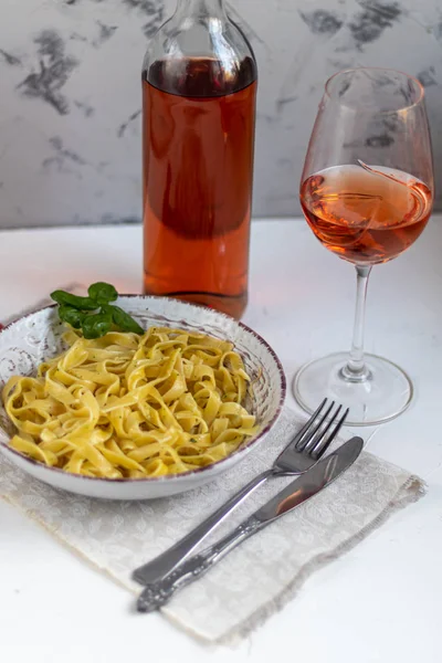 Italian pasta, spaghetti with avocado, spinach, basil, cream, cheese. Vegetarian vegetable pasta. Spinach with noodles. On a light background. In the background is a glass of orange wine. Copy space.