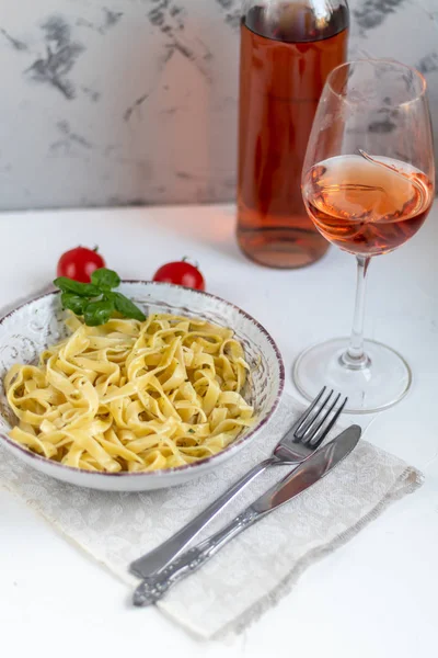 Italian pasta, spaghetti with avocado, spinach, basil, cream, cheese. Vegetarian vegetable pasta. Spinach with noodles. On a light background. In the background is a glass of orange wine. Copy space.