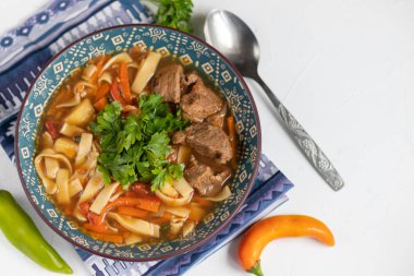 Doğu yemeği Lagman. Erişte, sığır eti, mavi, biber, domates. Yürekli yemek. Maydanoz ve kişniş ile süslenmiş. Hafif bir arkaplanda. Boşluğu kopyala.