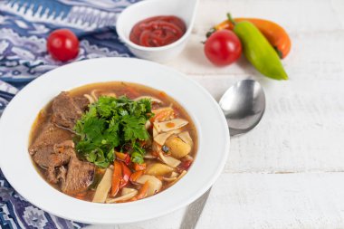 Doğu yemeği Lagman. Erişte, sığır eti, mavi, biber, domates. Yürekli yemek. Maydanoz ve kişniş ile süslenmiş. Hafif bir arkaplanda. Boşluğu kopyala.