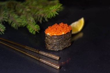 Siyah arka planda pirinç ve kırmızı havyarlı suşi gunkan. İyi yeni yıl ruhu. Yakınlarda Çin yemek çubukları var. Bir dilim limon. Arka planda bir ladin dalı var. Boşluğu kopyala. 