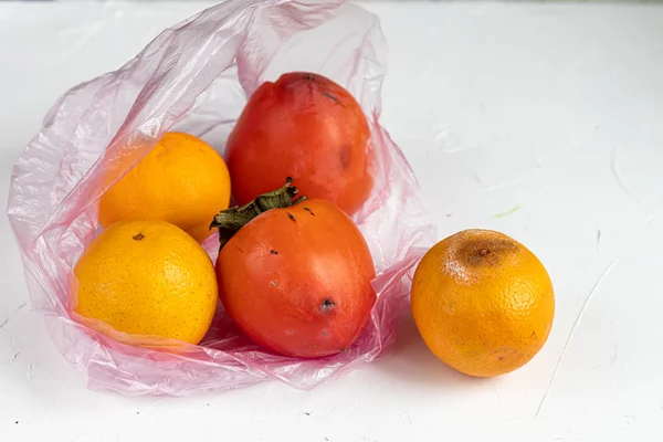 Environmentally harmful packages, spoiled fruits that lie in them. Ugly food. Copy space. Light background.