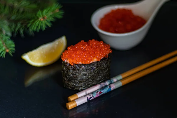 Siyah arka planda pirinç ve kırmızı havyarlı suşi gunkan. İyi yeni yıl ruhu. Yakınlarda Çin yemek çubukları var. Bir dilim limon. Arka planda bir ladin dalı var. Boşluğu kopyala. 