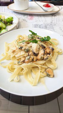 Kremalı soslu midyeli erişte. Arka planda taze sebze salatası var. Fotoğrafın dikey düzenlenmesi. Masa örtüsünde İngilizce yazılar var..