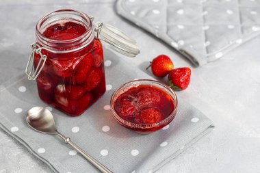 Cam kavanozda taze çileklerin yanında çilek reçeli. Gri bir arka planda. Ev yapımı kış meyvesi kurusıkı. Seçici odaklanma. Boşluğu kopyala
