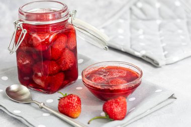 Cam kavanozda taze çileklerin yanında çilek reçeli. Gri bir arka planda. Ev yapımı kış meyvesi kurusıkı. Seçici odaklanma. Boşluğu kopyala