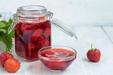 Strawberry jam in a glass jar next to fresh strawberries. On a white wooden background. Homemade winter fruit blanks. Selective focus. Copy space clipart