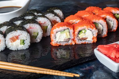 Bir kutu suşi Nigiri, Uramaki California, Philadelphia, siyah bir taş tabakta. Ahşap bir arka planda beyaz bir nakliye kutusunda suşi menüsü. Önplan.