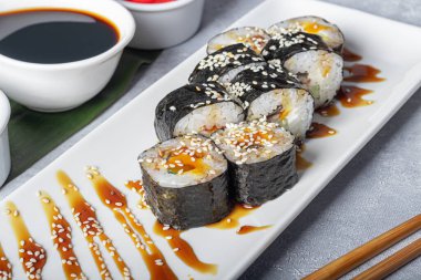 Suşi, Nigiri, Uramaki, California, Philadelphia 'yı beyaz bir tabağa koyar. Zencefil ve wasabi 'ye yakın. Beyaz kasede soya sosu. Açık gri arka planda. Boşluğu kopyala.