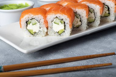 Suşi, Nigiri, Uramaki, California, Philadelphia 'yı beyaz bir tabağa koyar. Zencefil ve wasabi 'ye yakın. Beyaz kasede soya sosu. Açık gri arka planda. Boşluğu kopyala.