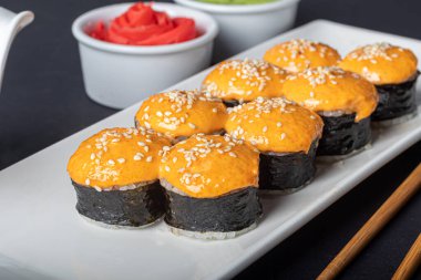 Suşi, Uramaki, California, Philadelphia 'yı beyaz bir tabağa koyar. Zencefil ve wasabi 'ye yakın. Beyaz kasede soya sosu. Karanlık bir arka planda. Boşluğu kopyala.