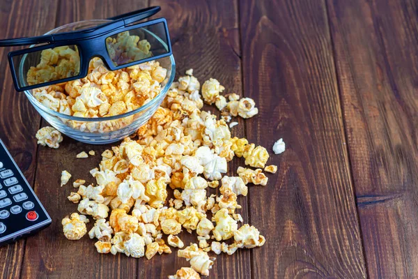 Ahşap bir yüzeyde şeffaf bir kase patlamış mısır. Laptop ve kulaklığın yanında. Maske virüslere karşı korur. Boşluğu kopyala.