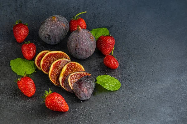 Fresh figs with strawberries on a dark background. Autumn dish. Casual autumn cuisine. Autumn harvest. copy space