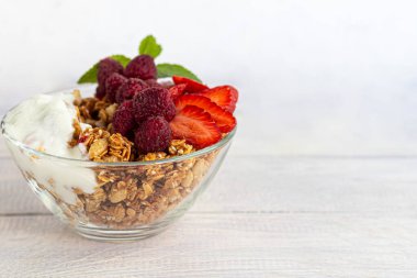 Ev yapımı tahıl gevreği, hafif tabakta çilek parçaları ve kavanozda yoğurt. Hafif bir arkaplanda. Vejetaryen yemeği. Sağlıklı kahvaltı. Boşluğu kopyala.