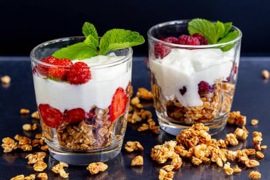 Koyu arkaplanda şeffaf bardakta çilek dilimli ev yapımı granola. Vejetaryen yemeği. Sağlıklı kahvaltı. Boşluğu kopyala.