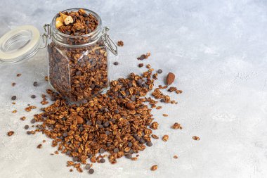 Çilekli granola, çikolata ve fındıklı cam kavanoz. Süt ya da yoğurt eklenerek. Gri bir arka planda. Vejetaryen yemeği. Boşluğu kopyala.