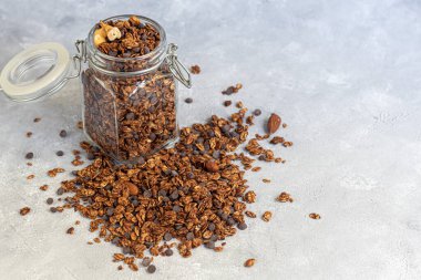 Çilekli granola, çikolata ve fındıklı cam kavanoz. Süt ya da yoğurt eklenerek. Gri bir arka planda. Vejetaryen yemeği. Boşluğu kopyala.