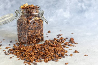 Çilekli granola, çikolata ve fındıklı cam kavanoz. Süt ya da yoğurt eklenerek. Gri bir arka planda. Vejetaryen yemeği. Boşluğu kopyala.
