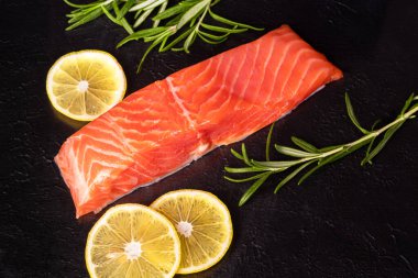 Hafif tuzlu alabalık. Taze balık filetosu. Mutfak malzemeleri, otlar ve limon. Siyah arka planda..