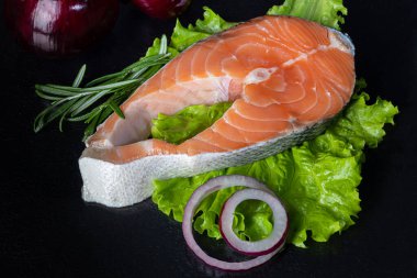 Taze somon bifteği. Mutfak malzemeleri, bitkiler, biber ve limonlu siyah arka planda balık filetosu. Boşluğu kopyala