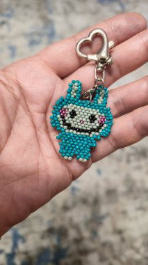 Hafif arka planda boncuklardan ve borazanlardan yapılmış el yapımı bir labubu oyuncağı. Anahtarlık ya da kolye yapar. Boşluğu kopyala