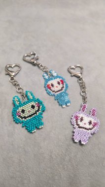 Hafif arka planda boncuklardan ve borazanlardan yapılmış el yapımı bir labubu oyuncağı. Anahtarlık ya da kolye yapar. Boşluğu kopyala