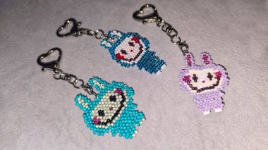 Hafif arka planda boncuklardan ve borazanlardan yapılmış el yapımı bir labubu oyuncağı. Anahtarlık ya da kolye yapar. Boşluğu kopyala