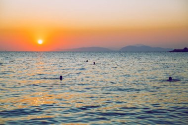 Yunan Cumhuriyeti. Denizde güneş ışığı ve yüzen insanlar. Dist olarak