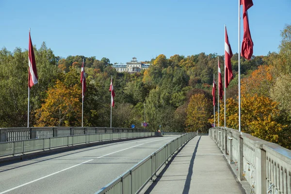 City Sigulda, Republika Łotewska. Rzeka i most z flagami w Au — Zdjęcie stockowe