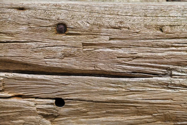 Texture of old wooden board with deep grooves, faded in the rain and sun outdoors. Trace from a rusty nail in the board