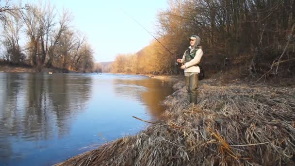 Una mujer atrapa un pez girando mientras está de pie en una orilla del río — Vídeos de Stock