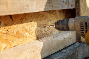 Bir işçi elektrikli matkap ile ahşap bir kiriş matkaplar