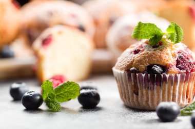 Taze pişmiş kek, pudra şekeri ve taze böğürtlen. Hafif arka planda taze yaban mersini ve ahududulu ev yapımı kekler. Ev yapımı pişirme konsepti. Yumuşak odak