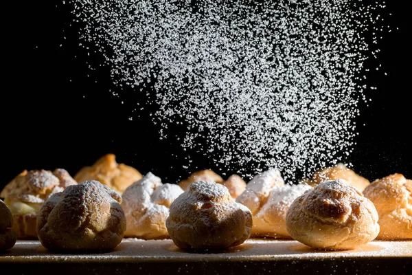 Ahşap bir tabağa krema serpiştirilmiş profiterol ve pudra şekeri serpiştirilmiş