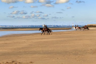DEAUVILLE, FRANCE 1 Eylül 2019: Bu bir sonbahar akşamında kıyı boyunca at süren kimliği belirsiz bir grup insan..