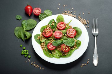 Salata bebek ıspanak yaprakları, yeşil mercimek, domates, zeytin yağı ve koyu bir yüzey üzerinde bir kapta limon suyu. Bir diyet yemek. Vejetaryen, vegan kavramı 