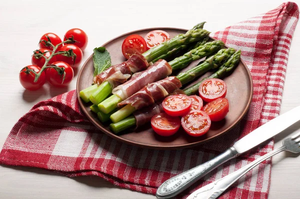 Asparagus with ham, tomatoes and egg poached in a in a clay plate.  Brown wooden background.  Light diet breakfast. Macro shooting