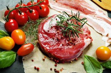 Parşömen kağıt üzerine çiğ et (biftek). Çok renkli domates ve fesleğen yaprakları yanında. Makro çekim.